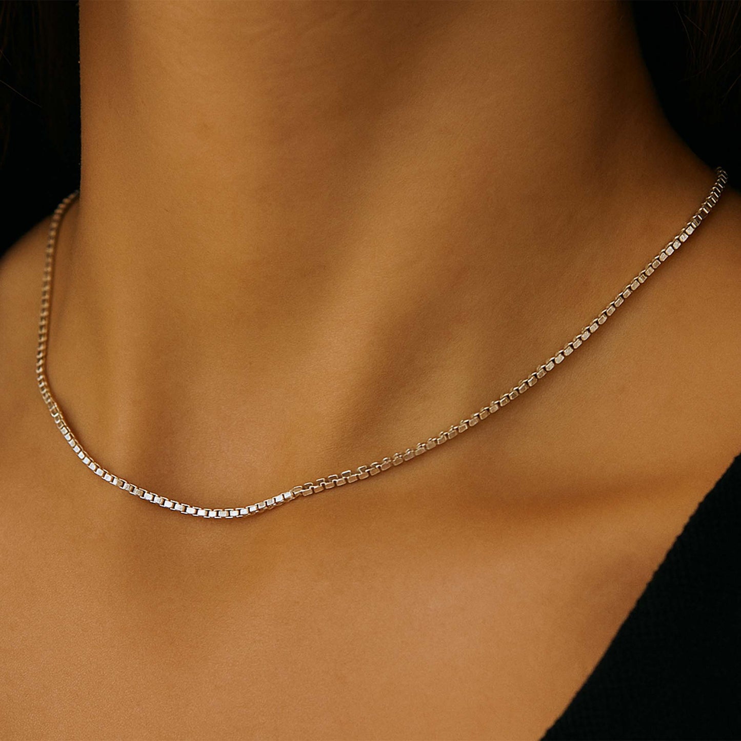 Silver chain necklace on a person's neck against a neutral background